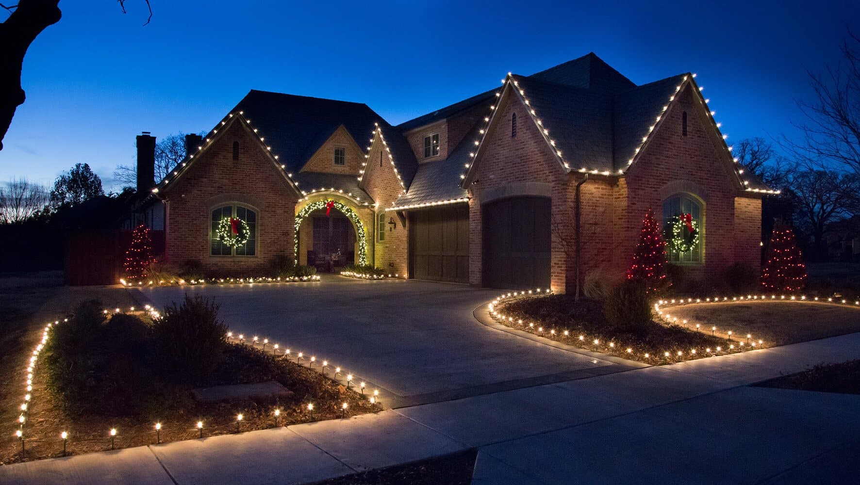 Full roofline lights, lit trees, and pathway lighting on a brick home